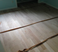 Installing wood flooring with adhesive and flooring straps