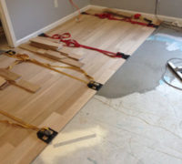 Installing wood flooring with adhesive and flooring straps