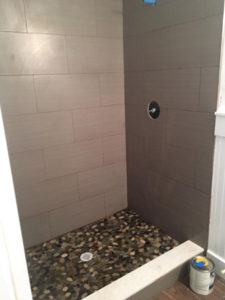 Wood look tile on standup shower walls with river rock floor