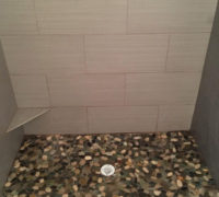 Wood look tile on standup shower walls with river rock floor